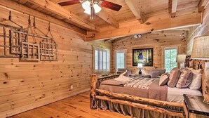 Interior de una cabaña de madera con una cama, un ventilador de techo y una ventana con persianas.