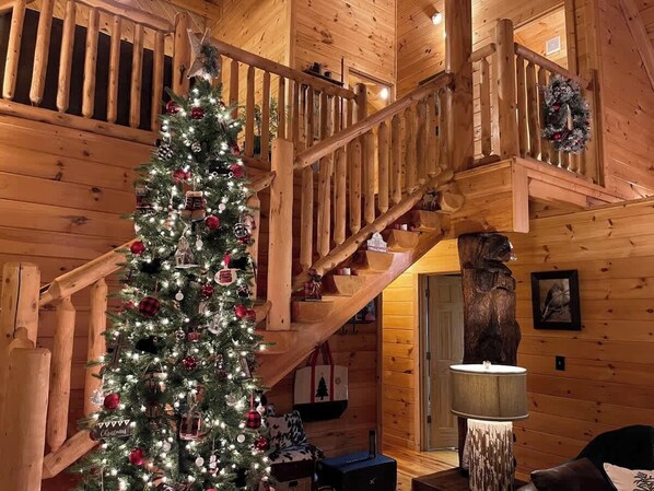 A wooden interior with a staircase, a Christmas tree, and a wooden sculpture.