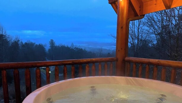 Un jacuzzi en una terraza de madera con vistas a árboles y colinas.