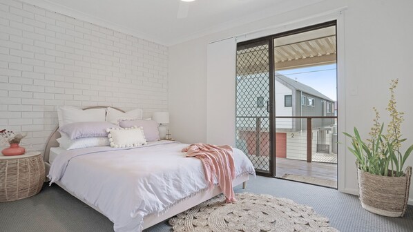 A bedroom with a bed, a bedside table, a lamp, a wicker basket, and a potted plant.