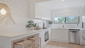 A modern kitchen with white cabinetry, a large window, and a built-in dishwasher.