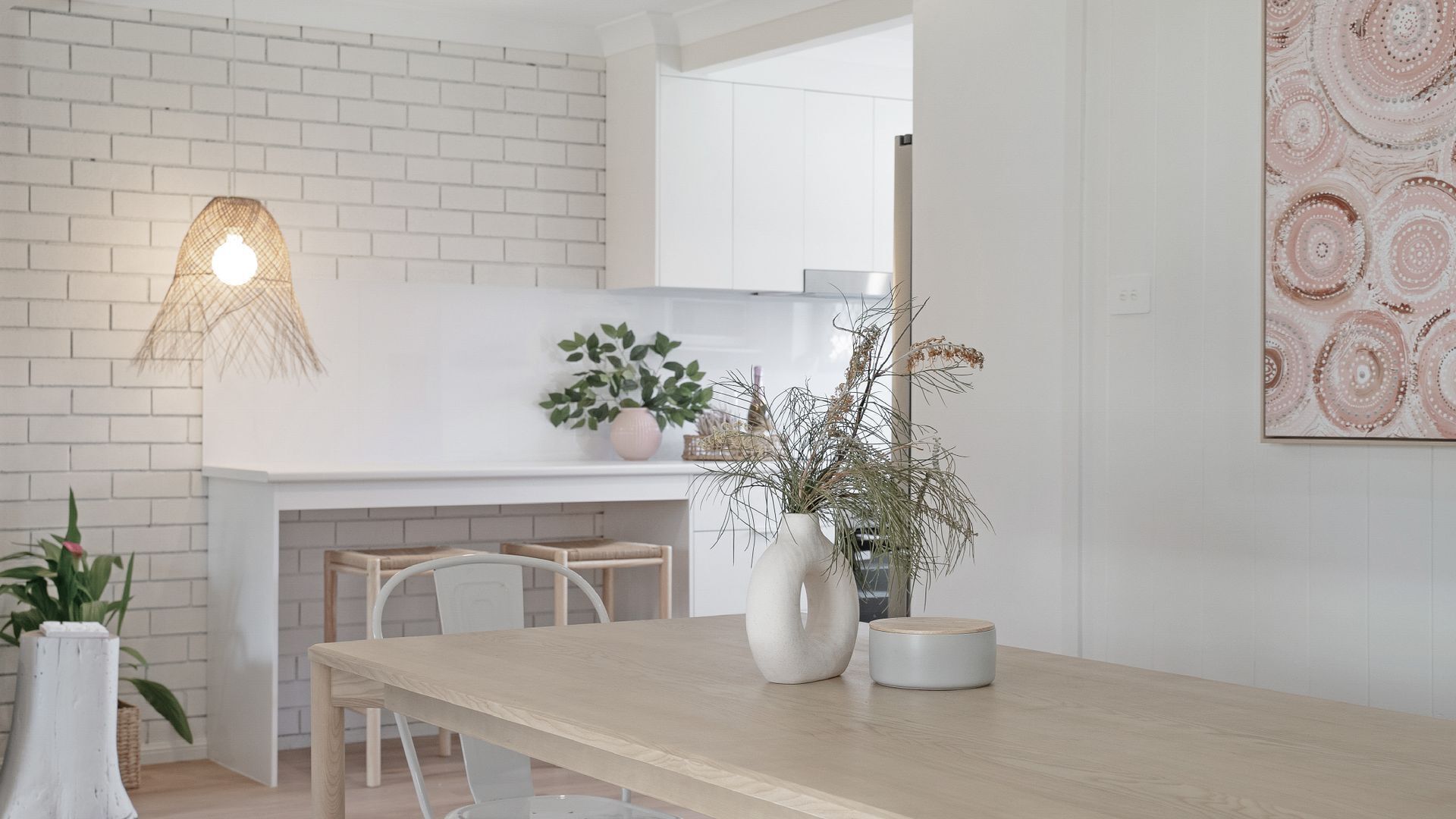 A modern kitchen with white brick walls, a wooden dining table, and a hanging light fixture.