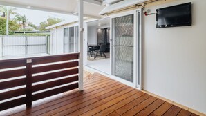 Un patio couvert avec une terrasse en bois, une porte-fenêtre coulissante donnant sur une salle à manger intérieure et un téléviseur à écran plat fixé au mur.