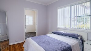 Une chambre à coucher comprenant un lit, une table de chevet, une commode et une fenêtre avec des stores.
