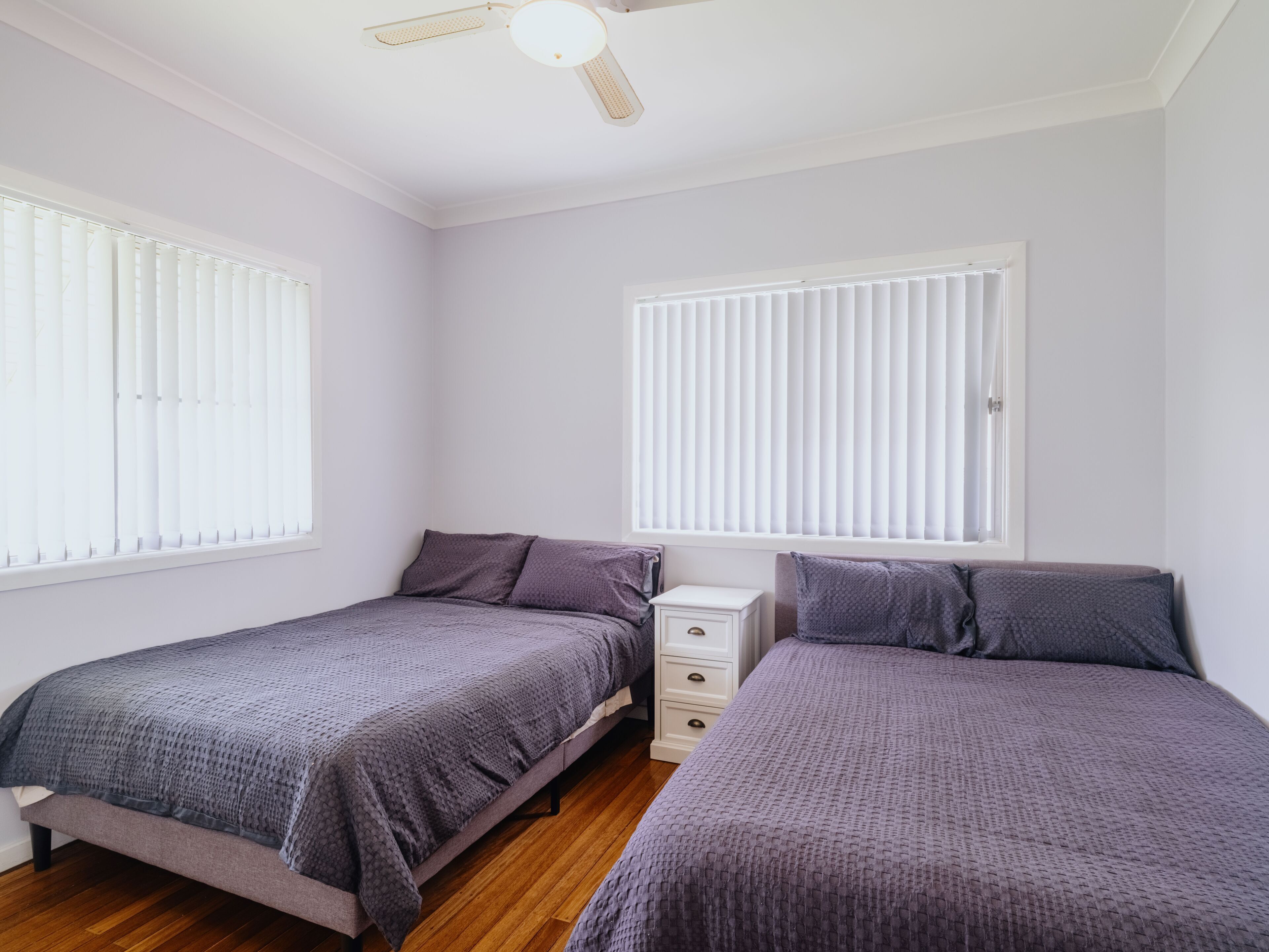 A bedroom with two beds, a nightstand, and a ceiling fan.