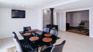 Un espace repas moderne avec une table en verre et des chaises noires, un poêle noir et un téléviseur à écran plat fixé au mur.