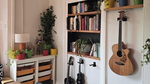 A room with a wooden dining table, chairs, a bookshelf, a wall clock, and a guitar. - Spacious 2 Bed/Bath Central Apt, Parking & Garden (Exeter)
