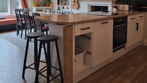 A modern kitchen with a central island, bar stools, a flat-screen TV, and a bookshelf. - Spacious 2 Bed/Bath Central Apt, Parking & Garden (Exeter)