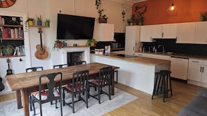 A modern kitchen with a central island, a dining area with a wooden table and chairs, and a living area with a sofa. - Spacious 2 Bed/Bath Central Apt, Parking & Garden (Exeter)