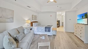 A modern bedroom with a bed, a sofa, a coffee table, a TV, and a ceiling fan. - Salt Therapy! Large Studio Unit w/ extra bedroom (St. Simons Island)