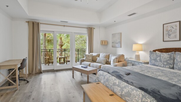 A spacious room with a large bed, a desk, and a balcony with outdoor furniture. - Salt Therapy! Large Studio Unit w/ extra bedroom (St. Simons Island)