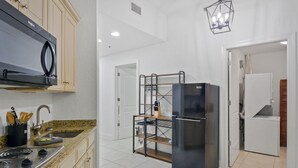 A kitchen with a stove, sink, and refrigerator. There is a wooden shelf unit and a hanging light fixture. - Salt Therapy! Large Studio Unit w/ extra bedroom (St. Simons Island)