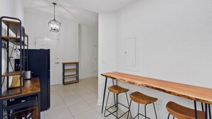 A kitchen with a wooden bar, stools, a hanging light fixture, and a door leading to another room. - Salt Therapy! Large Studio Unit w/ extra bedroom (St. Simons Island)