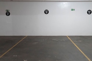 A parking garage with marked parking spaces and emergency exit signs. - CONDOMÍNIO SONHARE - 102 (Anapolis)