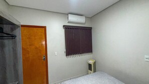 A room with a wooden door, a window with a dark curtain, a wall-mounted air conditioner, and a small heater. - CONDOMÍNIO SONHARE - 102 (Anapolis)