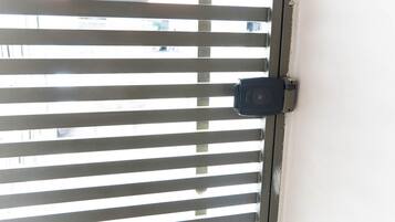 Una ventana con persianas horizontales y un objeto negro, posiblemente un candado o una manija, adherido al marco de la ventana.