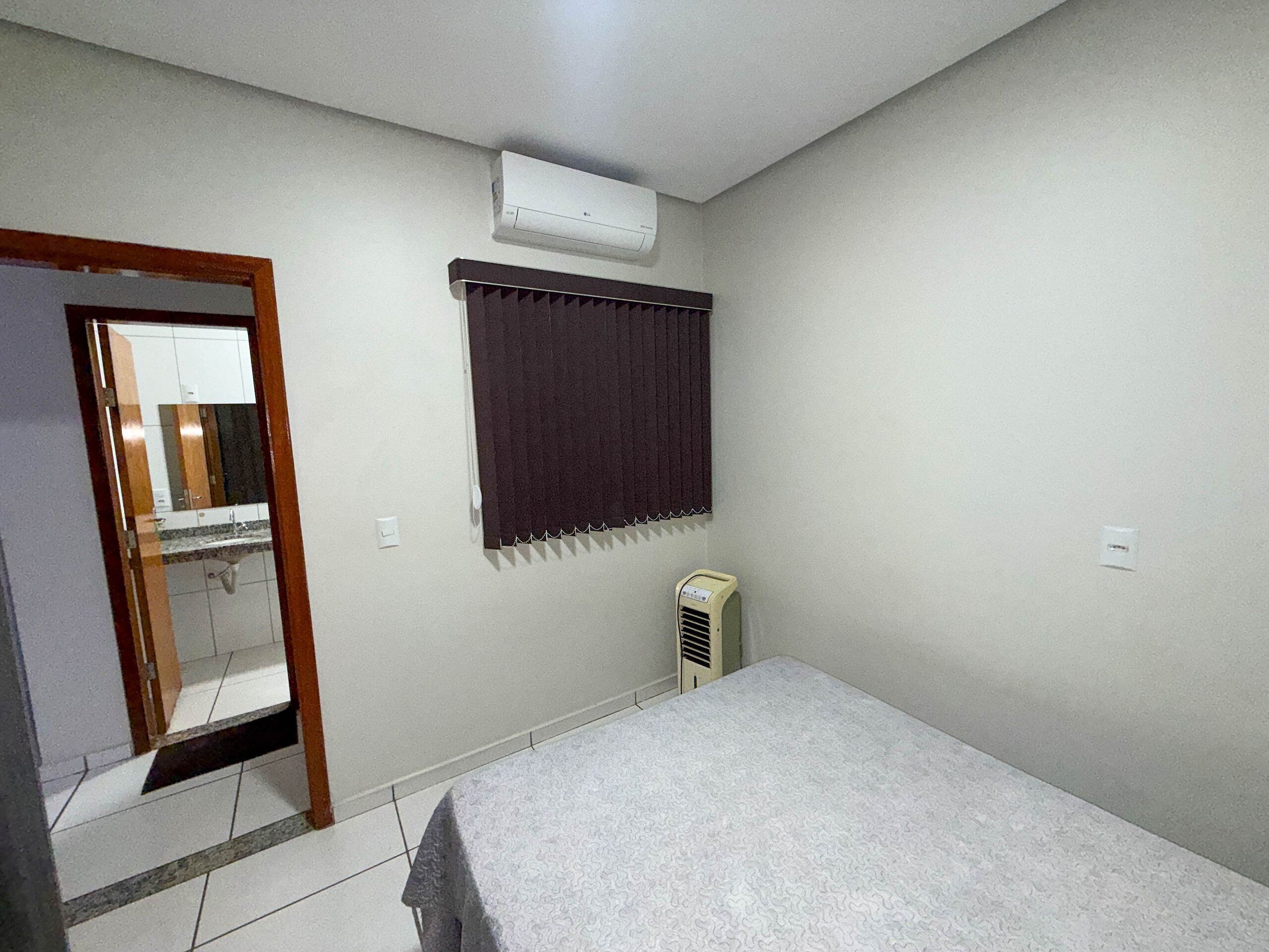 A bedroom with a bed, an air conditioner, a heater, a window with curtains, and a mirror.
