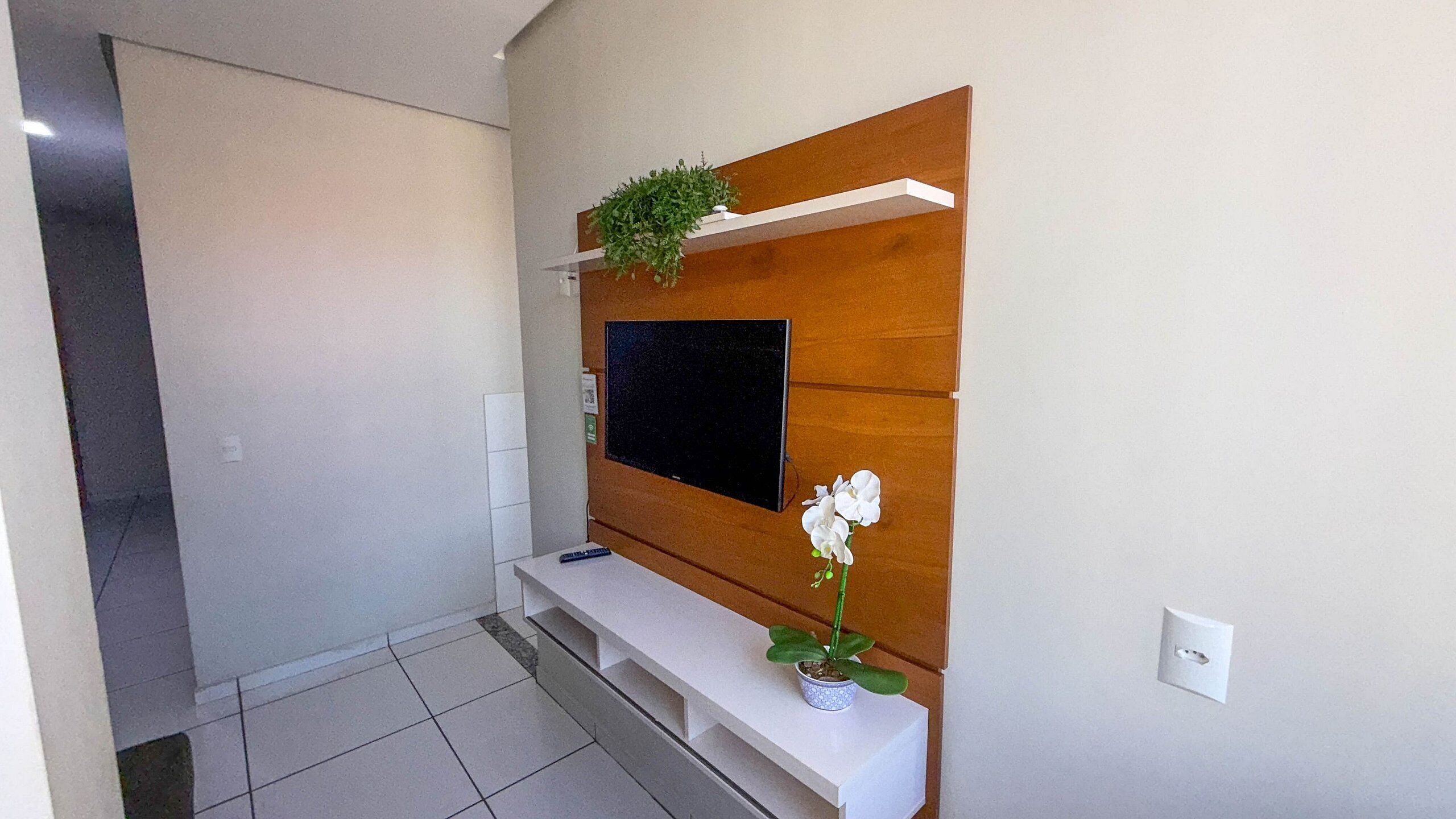 Ein modernes Wohnzimmer mit einem an einer Holzvertäfelung montierten Flachbildfernseher, einem kleinen weißen Konsolentisch und einer Topfpflanzen-Orchidee.