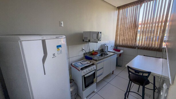 A compact kitchen with a refrigerator, microwave, stove, and a small dining area with a chair. - CONDOMÍNIO SONHARE - 102 (Anapolis)