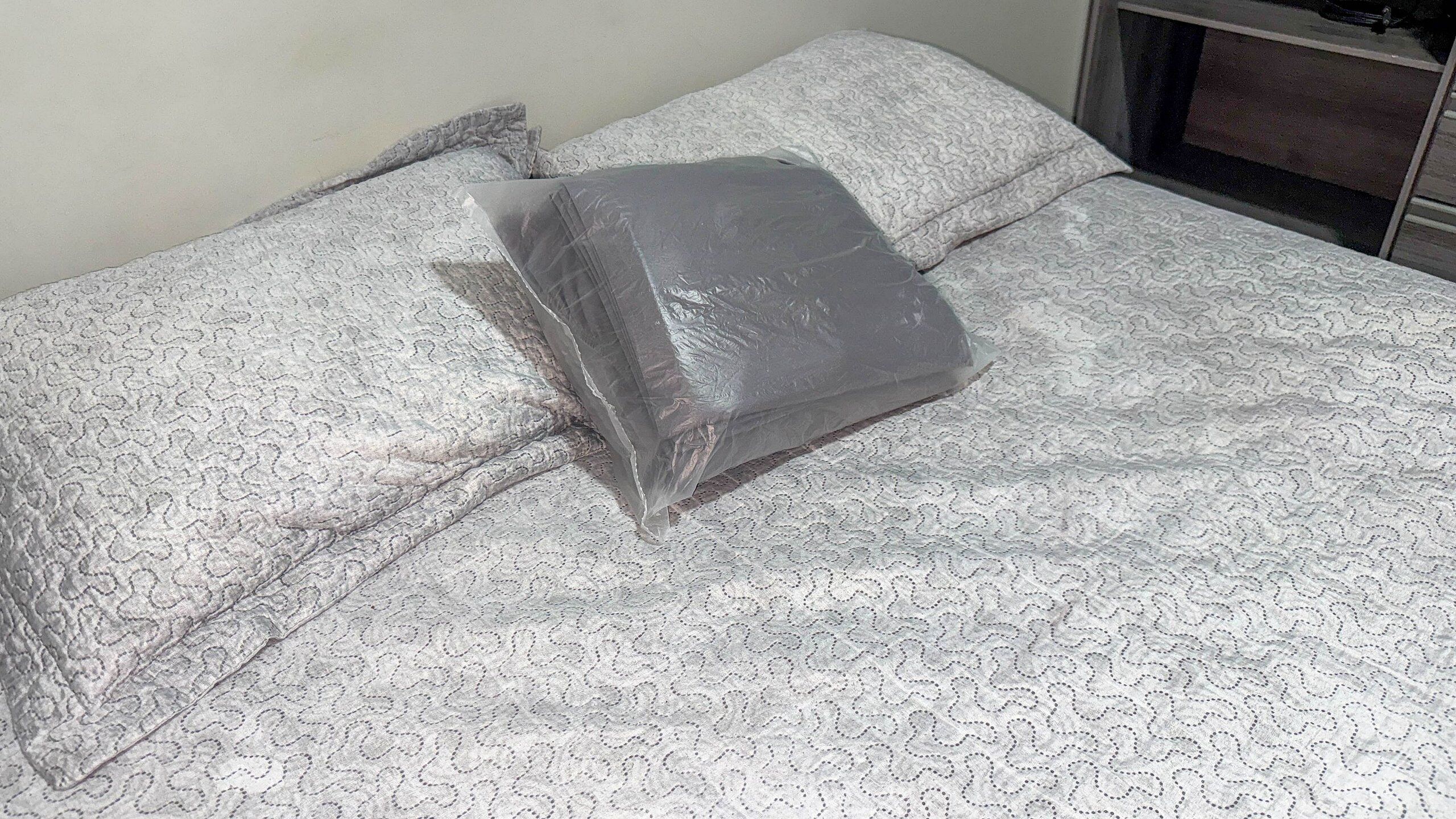 A bed with a patterned bedspread and a plastic bag on it.