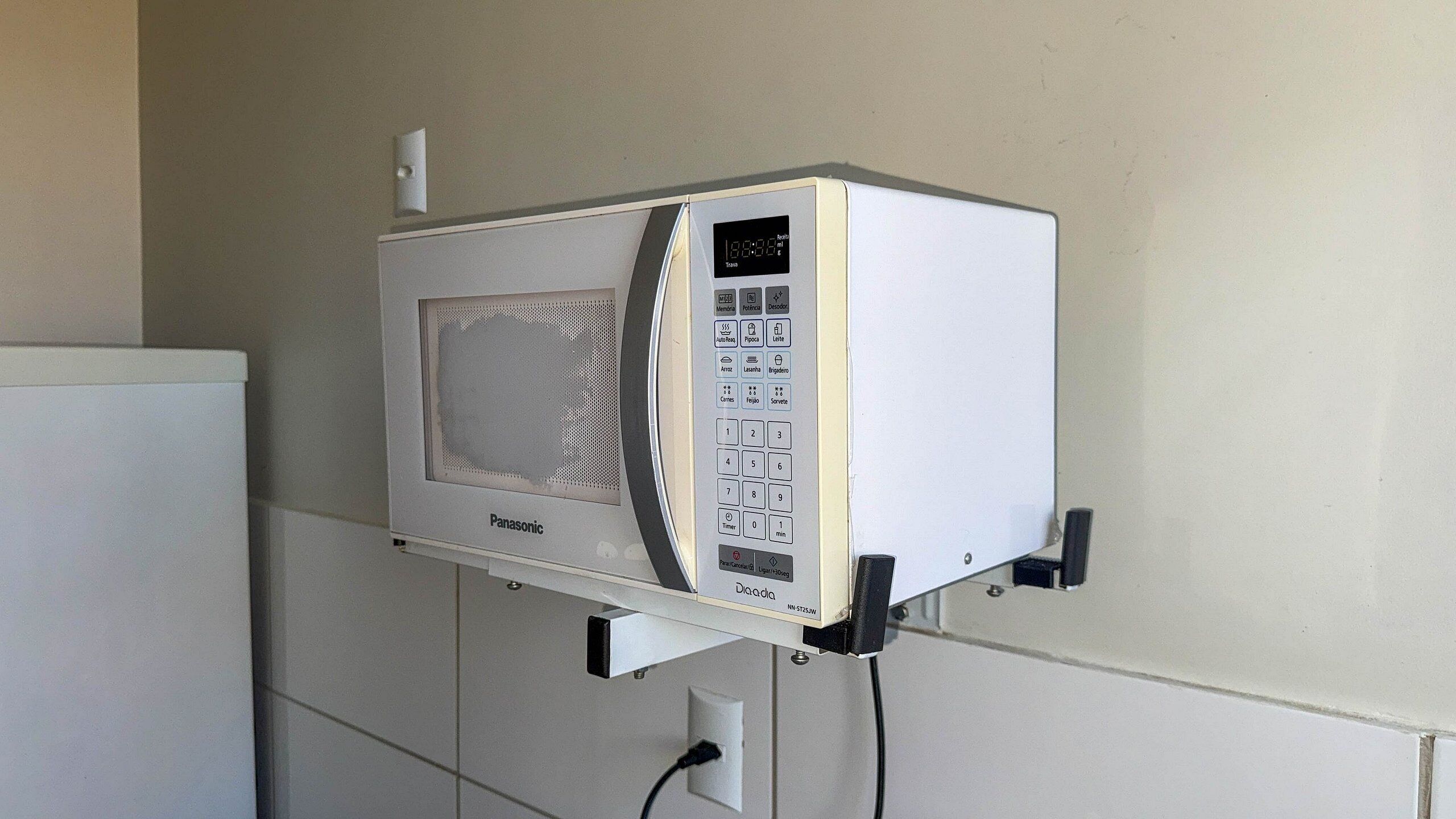 A microwave oven mounted on a wall with a control panel, a power cord, and a brand name 'Panasonic'.