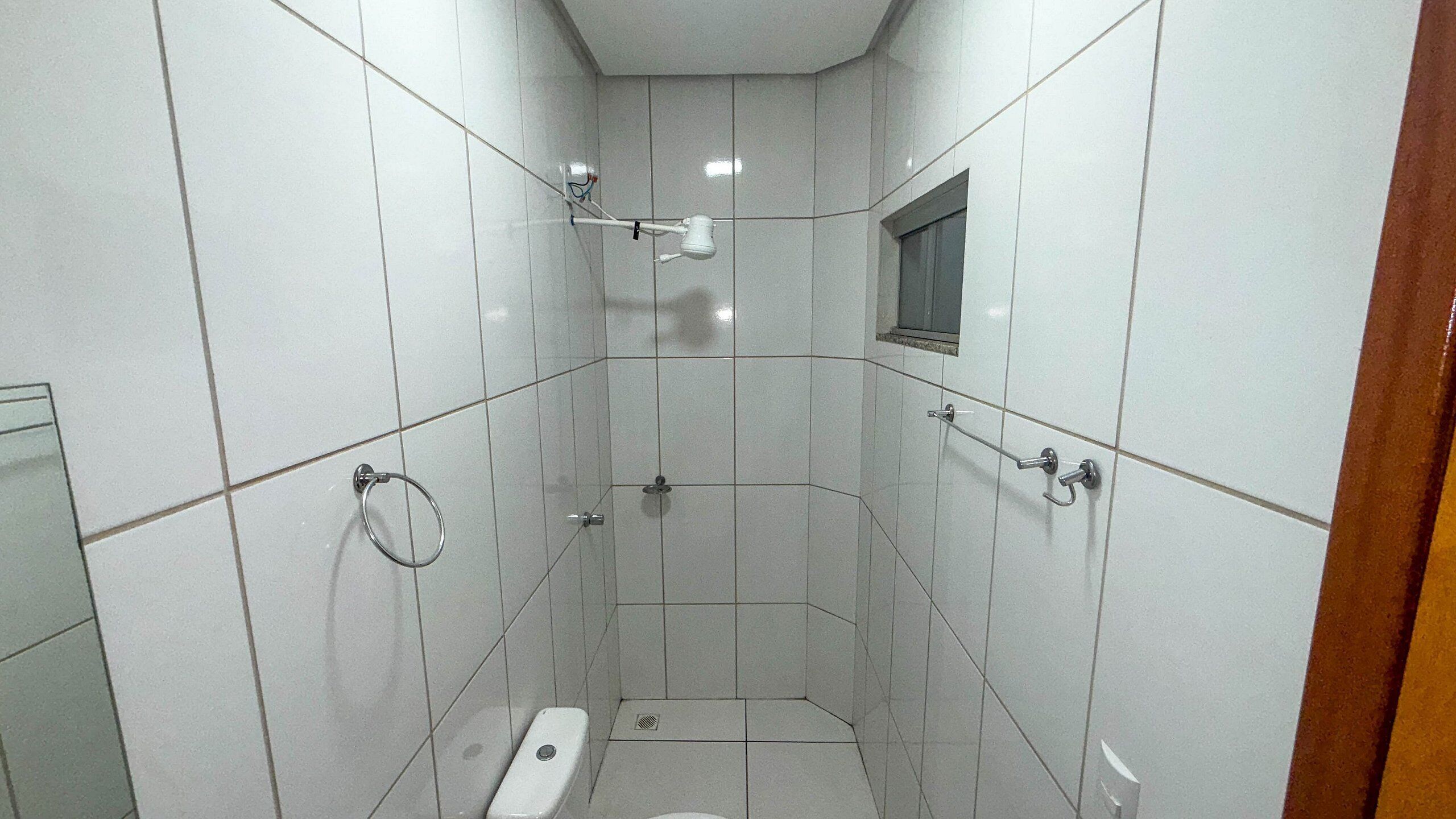 Casa de banho pequena com azulejos, um sanitário, um chuveiro e uma janela.