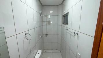 Casa de banho pequena com azulejos, um sanitário, um chuveiro e uma janela.