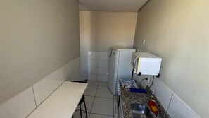 Una pequeña cocina americana equipada con refrigerador, microondas y pileta.
