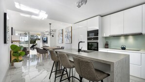 Una cocina moderna con gabinetes blancos, encimera de mármol y taburetes de bar.
