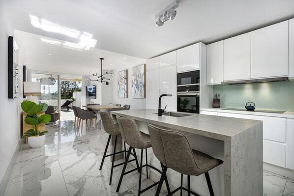 A modern kitchen with white cabinets, a marble countertop, and bar stools. - Spectacular, luxurious apartment near the beach (San Pedro de Alcántara)