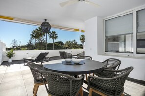 A round table with wicker chairs, a ceiling fan, and a view of palm trees and a white building. - Spectacular, luxurious apartment near the beach (San Pedro de Alcántara)