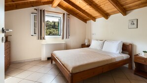 Un dormitorio con techo de madera, una cama con ropa de cama blanca, una mesita de noche y un radiador. Cortinas en la ventana.