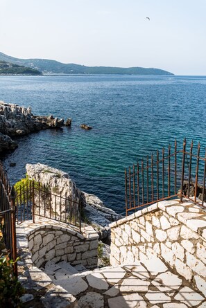 A coastal stone pathway leading to a rocky shoreline with a metal fence. - Four-Bedroom Villa Alexandros (Corfu)