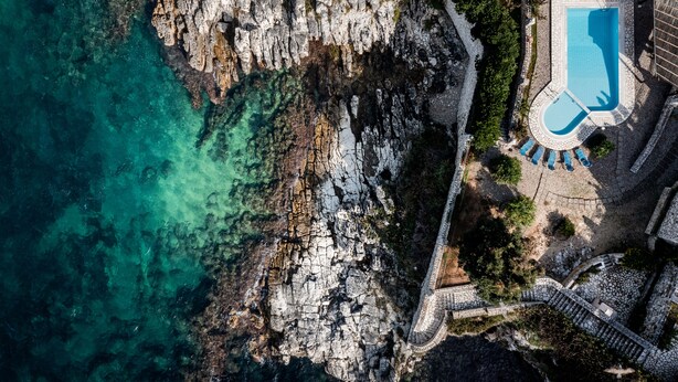 Vista aérea de una propiedad costera con piscina, acantilados rocosos y un camino de piedra que lleva a la piscina.