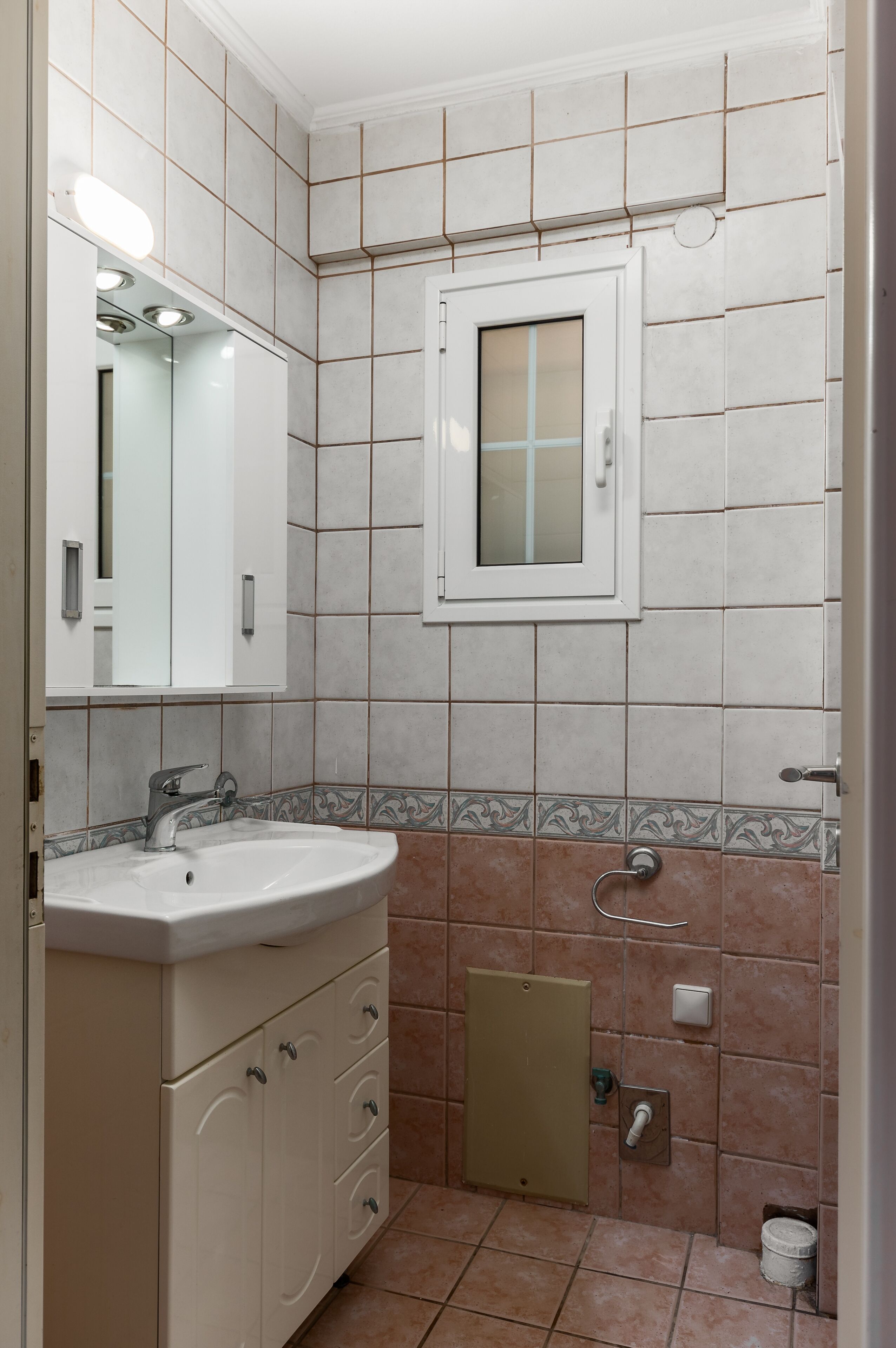 A bathroom with a sink, mirror, cabinet, and a window.