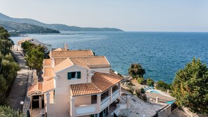 Una propiedad costera con una casa grande de techo de tejas, piscina y vista al mar.