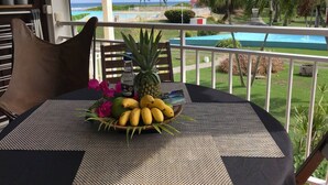 A table with a tropical fruit bowl, a bottle, and a menu on a balcony overlooking a pool and palm trees. - Anse des Rochers lovely "1,2,3 Soleil" studio with superb sea view. (Saint Francois)