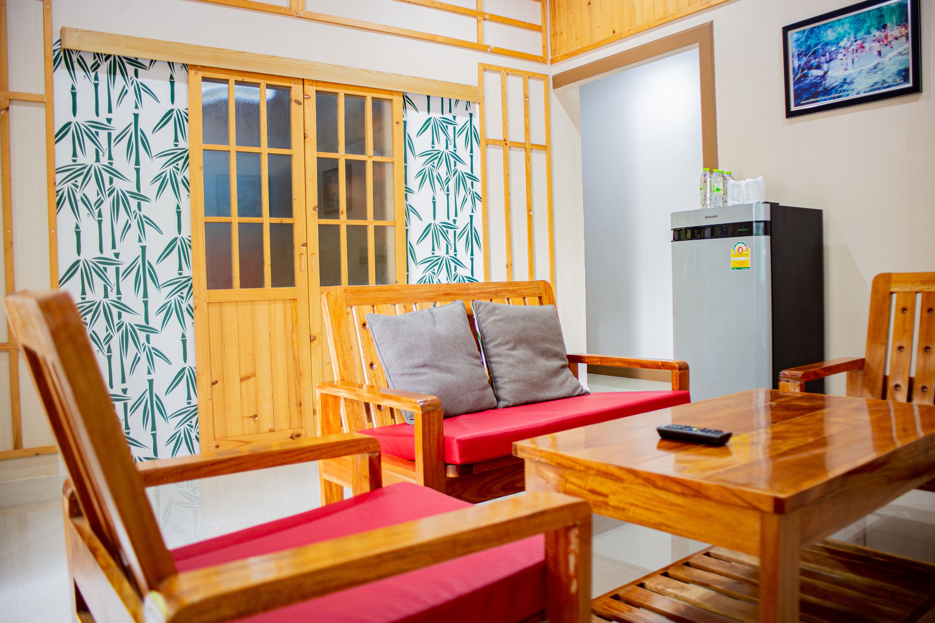 Una habitación con sofá de madera, cojines rojos, una mesa de comedor de madera y un refrigerador.