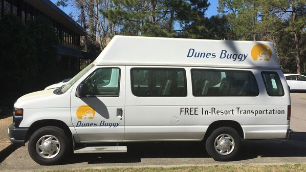 Una camioneta blanca con la leyenda 'Dunes Buggy' y 'Transporte gratuito en el resort', estacionada al aire libre.