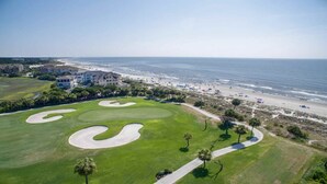 Um campo de golfe com bunkers de areia, praia e vista para o oceano.