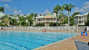 En swimmingpool med kristallklart blått vatten, omgiven av palmer och ett vitt staket.