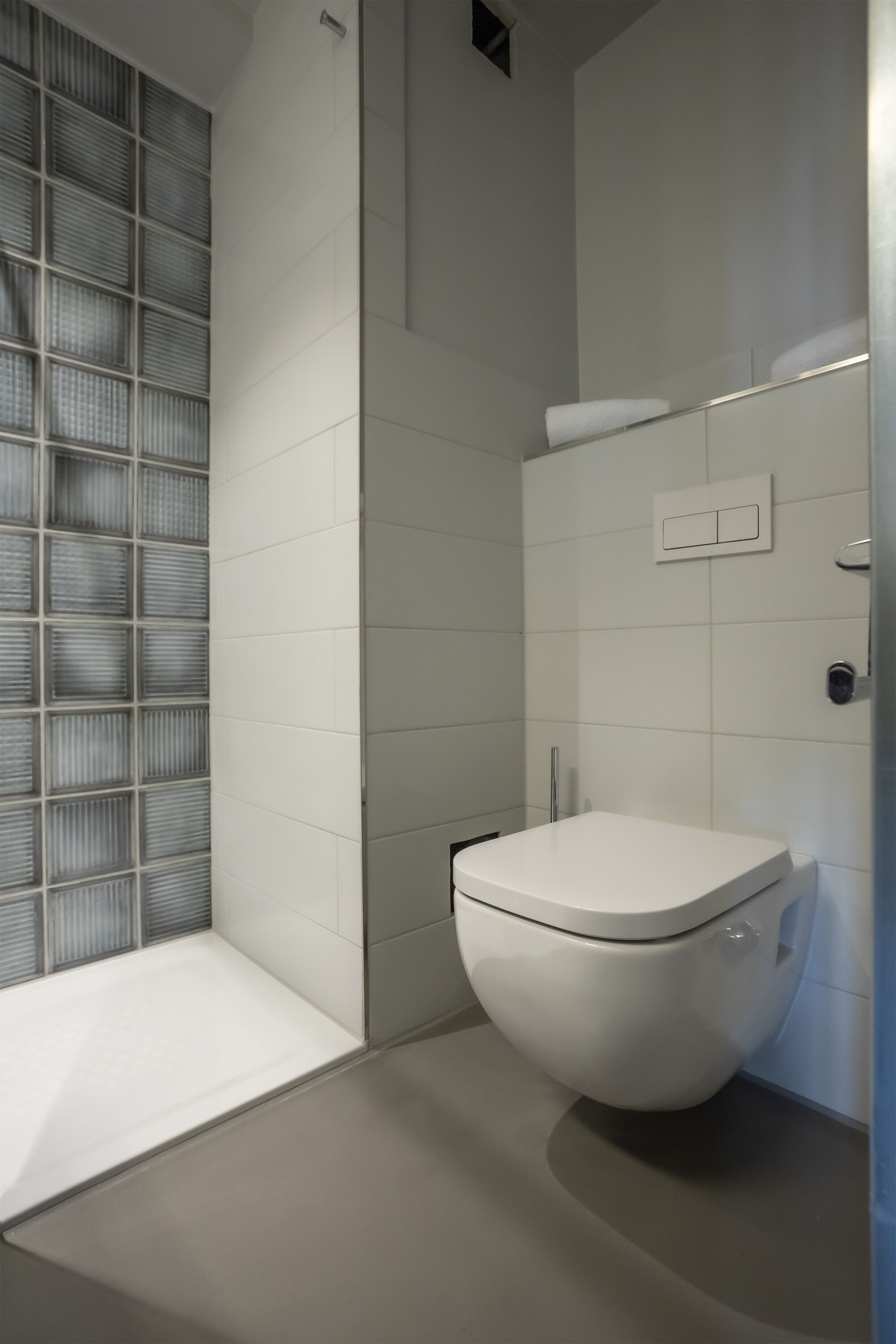 A modern bathroom with a white toilet, a shower area with a glass door, and a wall-mounted sink.