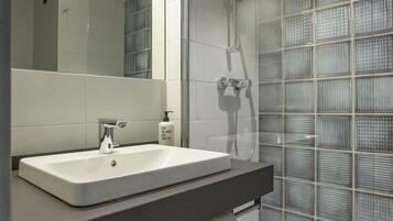 Ein modernes Badezimmer mit einem großen Spiegel, einem weißen Waschbecken, einer Dusche mit Glastrennwand und einem Handtuchhalter.
