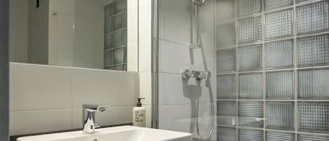 A modern bathroom with a large mirror, a white sink, a shower with glass panels, and a towel rack.