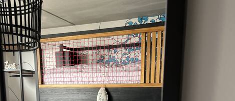 Una cama litera con estructura de madera y una cama inferior con colchón blanco y almohada azul.