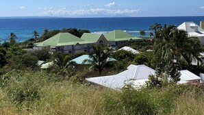 A coastal view with multiple buildings, some with green roofs, and palm trees. - Anse des rochers, very pretty "Bamboo" studio 30 meters from the beach. (Saint Francois)