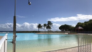 A clear view of a swimming pool with a metal railing, palm trees, and a gazebo in the background. - Anse des rochers, very pretty "Bamboo" studio 30 meters from the beach. (Saint Francois)