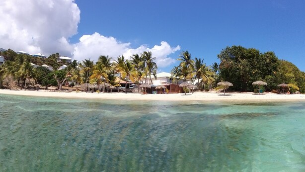 A beach resort with clear turquoise waters, a sandy beach, and a backdrop of lush greenery and palm trees. - Anse des rochers, very pretty "Bamboo" studio 30 meters from the beach. (Saint Francois)