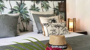 A bed with a tropical-themed headboard, pillows, a straw hat, and a vase with flowers. - Anse des rochers, very pretty "Bamboo" studio 30 meters from the beach. (Saint Francois)