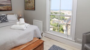 A bedroom with a large window, a bed, a bedside table, a lamp, and a map on the wall.